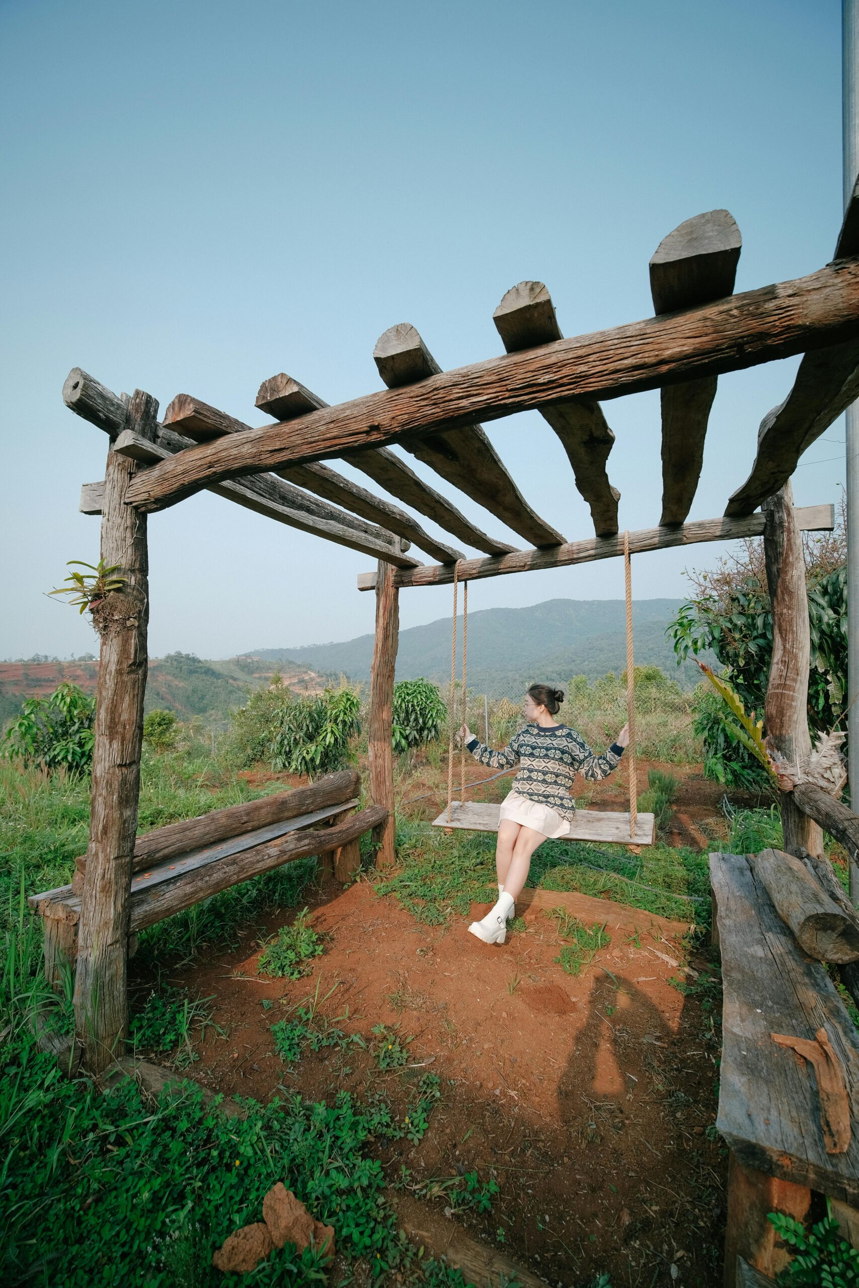 Woman enjoying a serene swing under a rustic pergola with mountain views.